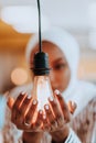 Sentimental portrait of African-American young female Muslim wearing hijab while holding a lightbulb.