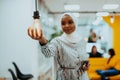 Sentimental portrait of African-American young female Muslim wearing hijab while holding a lightbulb.