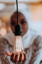 Sentimental portrait of African-American young female Muslim wearing hijab while holding a lightbulb.