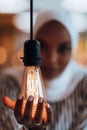 Sentimental portrait of African-American young female Muslim wearing hijab while holding a lightbulb.