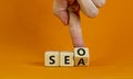 SEO vs SEA. Businessman turns a cube and changs words `SEA - search engine advertising` to `SEO - search engine optimization`. Royalty Free Stock Photo