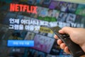 Seoul, south Korea - May 20, 2020: Man`s hand operating remote control towards television with Netflix screen on