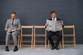 Separating the competition. Shot of a row of chairs with two businessmen seated slightly apart.