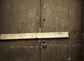 sepia close up of an old cracked peeling wooden plank door barred shut with a piece of timber and rusty nails with a lock and Royalty Free Stock Photo