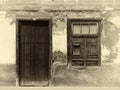 Sepia image of the facade of an old spanish house with shuttered window and old wooden door with faded plaster walls in strong s Royalty Free Stock Photo