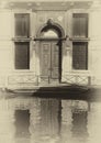 Sepia image of an old building along a canal in venice with shutters and doorway reflected in the water in bright sunlight and s Royalty Free Stock Photo