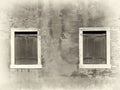 Sepia image of vintage distressed painted wall with two wooden shuttered windows with white surrounds in bright sunlight