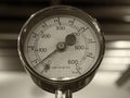 Sepia monochrome image of an old shiny brass round pressure gauge with a round dial marked in numbers