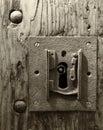 Sepia monochrome large square rusty iron lock with keyhole in an old wooden door and metal rivets