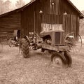 Sepia shot of an antique tractor in front of a barn with a variety of vintage farming equipment