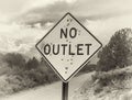 A sepia tones image of a road sign stating No Outlet riddled with bullet holes