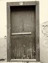 Sepia vintage style image of a closed wooden door locked and barred shut with nails with peeling paint and stone surround