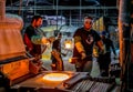 Workers carry crucible ladles of melted glass