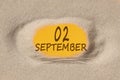 September 2. 2th day of the month, calendar date. Hole in sand. Yellow background is visible through hole