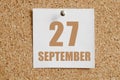 september 27. 27th day of the month, calendar date.White calendar sheet attached to brown cork board.Autumn month, day