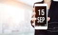 September 15th. Day 15 of month, Calendar date. White smartphone with Calendar date in businesswoman hand on blurred background.