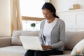 Serene black girl sit on sofa and work on laptop