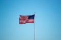 A serene, cloudless sky of red, white and blue provides a patriotic backdrop for an American flag waving in the wind on its pole.