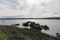 Serene Coastal View: Rocky Shoreline with a Distant Lighthouse Under a Cloudy Sky