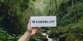 Motivational inspiring hand holding word card wanderlust in woods