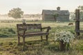 Serene farm scene with a wooden bench, flowers, and grazing horses at sunrise Royalty Free Stock Photo