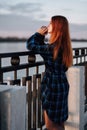 Serene girl standing alone on waterfront in front of fence of embankment.