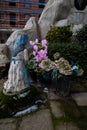 Serene Graveside Scene: Flower-Adorned Tomb with Woman Statue and Building Background