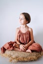 Serene little girl in a dress meditating on a pillow in a tropical style room