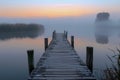 Serene Misty Lake at Sunrise with Wooden Pier Leading into Calm Waters and Ethereal Foggy Landscape Background Royalty Free Stock Photo