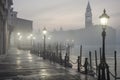 A serene, misty Venice scene at dawn with illuminated lampposts, a wet dock, and historical buildings emerging from the fog Royalty Free Stock Photo
