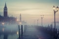 A serene, misty Venice scene at dawn with illuminated lampposts, a wet dock, and historical buildings emerging from the fog Royalty Free Stock Photo