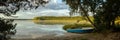 Serene morning landscape. panoramic view from the shore of a large lake with a fishing boat, sky reflection on the water, a forest Royalty Free Stock Photo