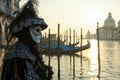 A serene morning at the Venetian Carnival, a lone figure in a traditional mask and costume, standing by the edge of a canal with Royalty Free Stock Photo