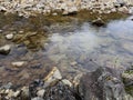 A serene and natural landscape featuring a clear, shallow stream flowing over a bed of multicolored rocks and pebbles. Royalty Free Stock Photo