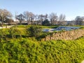 Serene park landscape featuring a stone wall, vibrant greenery, and a partially visible tiled structure, possibly an old pool or Royalty Free Stock Photo