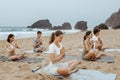 Serene people. Young women and men on yoga class doing meditation lotus pose on the beach