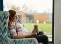 Beautiful woman expecting a baby, sitting on the armchair and dreamily looking at a cuddly rabbit toy. Pregnant woman relaxing at