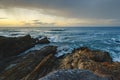 A serene rocky beach is bathed in the warm hues of a sunset, with dramatic clouds in the background