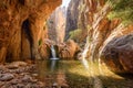 Serene rocky canyon with a small waterfall and crystal-clear water pool surrounded by sunlit cliffs and scattered greenery in a Royalty Free Stock Photo
