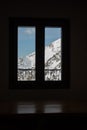 A serene scene of snow-capped mountains bathed in soft light, framed by a window.