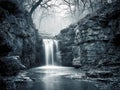 Serene small waterfall cascading over rocky cliffs into a calm pool surrounded by leafless trees in a misty forest during Royalty Free Stock Photo