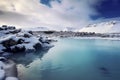 A serene snowy landscape with a vibrant blue lake, surrounded by snow-covered rocks and mountains under a cloudy sky Royalty Free Stock Photo