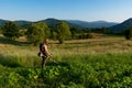 Serene Sunset Harvest: Farmer Taming the Tall Grass with Trimmer in Vegetable Garden