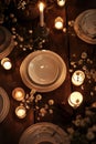 Serene table setting at night with dark wooden tablecloth, white plates, candles and flowers. Elegant dinner atmosphere with fine