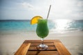 Serene tropical island scene with green coloured cocktail on a bench against a tropical beackground