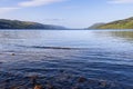 Loch Ness presents a serene view under clear skies, with its vast water expanse bordered by sloping green hills