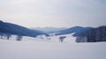 A serene winter landscape with rolling hills, snow-covered fields, and distant mountains Royalty Free Stock Photo