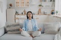 Serene woman practices yoga meditation sitting on cozy couch at home. Wellness, stress relief Royalty Free Stock Photo