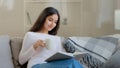 Serene young girl student daughter relaxed arabian biracial intelligent woman sits on sofa reads paper book scientific