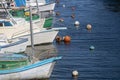 Series of boats floating in the calm waters of a bay or harbor, marked by bright buoys
